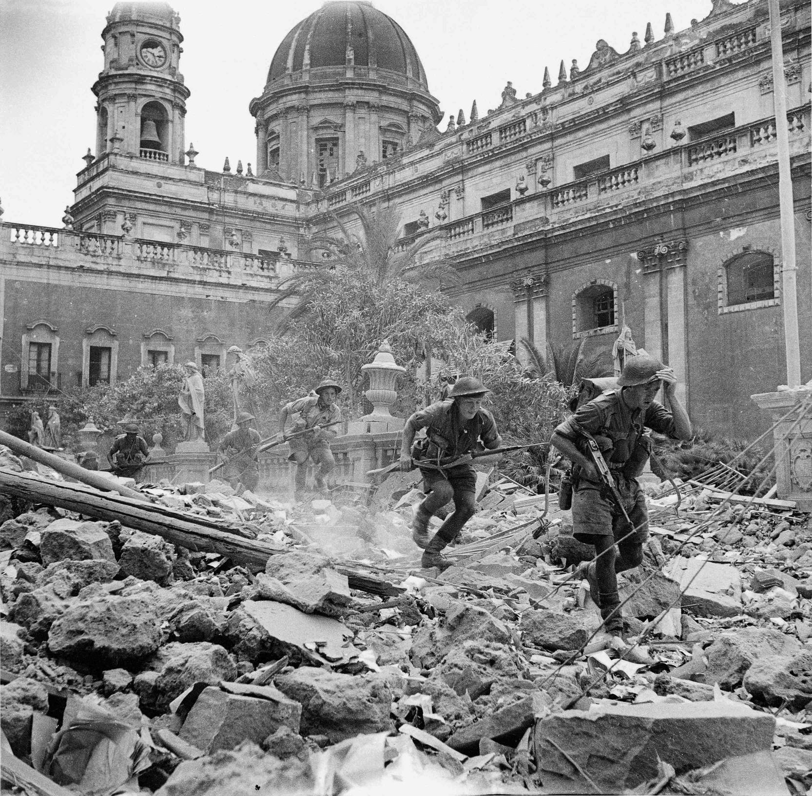  Британски бойци минават през руини в Катания, където настъплението на Монтгомъри се забавя. Ген. Алекзандър заповядва на Патън да подходи към Месина от запад, само че и той напредва постепенно, тъй като се натъква на по-непропусклива отбрана, в сравнение с в Палермо 